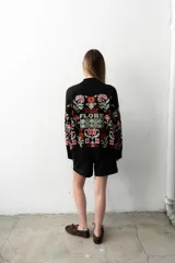 Buzo tejido de algodón negro con diseño jacquard de flores multicolor, cuello en V y mangas largas.