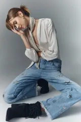 Jean de tiro alto en denim azul rígido, con lavado localizado, bigotes y apliques de estrellas brillantes. Presenta pierna recta y ruedo desflecado.