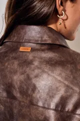 Campera de cuero vegano en tono marrón con acabado desgastado, corte recto y cierre frontal con botones a presión. Presenta cuello clásico y diseño minimalista.