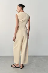 Chaleco color beige confeccionado en tejido de punto elástico, con escote en V, sin mangas y bajo acabado en línea evasé con cierre frontal de botones.