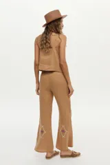 Pantalón camel de lino, de corte recto y tiro alto, con detalles bordados en la parte inferior de las piernas.