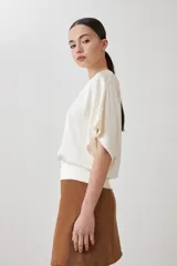 Blusa color beige de tela satinada, con escote barco y mangas cortas.