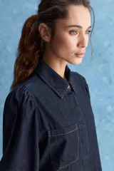 Camisa de jean azul oscuro con calce relajado, cuello clásico, bolsillo aplicado en el delantero y mangas largas abullonadas con puños abotonados.