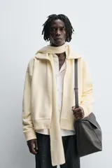 Sudadera color crema de algodón con interior afelpado, corte relajado, cuello subido y manga larga. Presenta bolsillos de vivo en la cadera y acabados en rib, con cierre frontal de cremallera.