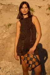 Vestido corto de tejido de punto con lúrex, sin mangas y cuello a la base. Presenta apliques decorativos en forma de flores en el frente y un pequeño tajo en el ruedo.