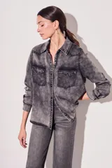 Camisa de denim celeste con cuello clásico, cierre frontal con botones a presión, dos bolsillos con solapa abotonada en el pecho y mangas largas con puños abotonados.