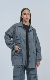 Campera gris de tejido liviano, con cuello camisero, cierre frontal de broches y puños elásticos. Presenta múltiples bolsillos cargo en el frente con ribetes reflectantes blancos.