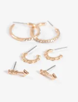Set de tres pares de aros dorados: un par de aros tipo argolla con strass, un par de aros pequeños con diseño calado y un par de aros con forma de flecha.