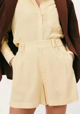 Short de corte recto y tiro alto, confeccionado en tela de lino color amarillo claro. Presenta cintura con elástico en la parte posterior, trabillas para cinturón y bolsillos laterales.