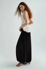 Top halter color blanco con estampado de lunares negros, escote en V pronunciado y detalle fruncido en la cintura con vuelo tipo peplum.