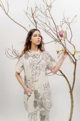 Vestido corto beige con estampado botánico en negro, cuello camisero, mangas cortas y cierre frontal con botones.