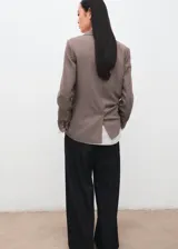 Blazer de corte recto y silueta estructurada, con cuello solapa y cierre frontal de botones. Presenta un diseño de estampado micro-cuadros en tonos tierra.