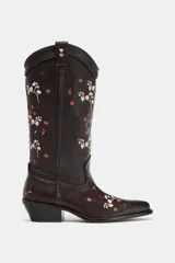Bota estilo cowboy de cuero marrón oscuro con bordados florales en tonos claros y rojizos. Presenta tacón ancho en bloque, puntera afilada y tiradores laterales para facilitar el calce.