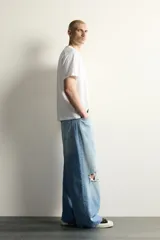 Jeans baggy fit de corte holgado en denim de algodón celeste, con tiro medio, cinco bolsillos, roturas en las rodillas y cierre frontal con cremallera y botón.