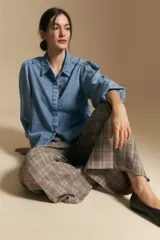 Camisa de denim azul con cuello camisero, cierre frontal de botones y mangas largas abullonadas con hombros fruncidos.