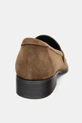 Mocasín de mujer confeccionado en serraje color marrón, con detalle de antifaz en el empeine, costuras a la vista y punta redonda. Cuenta con un pequeño tacón cuadrado.