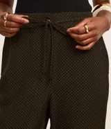 Pantalón fluido de cintura alta, confeccionado en crepé, con elástico y lazo en la cintura. Presenta un estampado geométrico con líneas curvas horizontales.