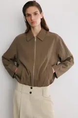 Cazadora tipo bomber color marrón, confeccionada en mezcla de viscosa. Tiene cuello solapa, manga larga, bolsillos de vivo en los laterales y bajo acabado en elástico. Cierre frontal con cremallera metálica.