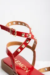 Sandalias rojas de charol con tiras finas, puntera cuadrada y cierre con hebilla al tobillo. Decoradas con tachas piramidales doradas.