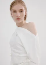 Blusa blanca de algodón con cuello asimétrico, detalles fruncidos, manga larga y cierre de cremallera lateral.