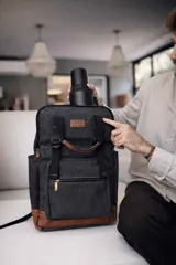 Mochila matera y porta notebook en tela canvas de color marrón, con diseño funcional que incluye bolsillo frontal con cierre, correas ajustables, manija superior y detalles de tiras de lona con hebillas metálicas.