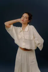 Campera liviana de lino en color beige, con cuello camisero, cierre frontal de botones, mangas largas amplias y bolsillos con solapa en el pecho.