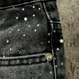 Pantalón de jean negro con corte flare, decorado íntegramente con apliques de cristales brillantes. Presenta cierre frontal con botón y bolsillos clásicos.