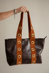 Cartera tipo tote de cuero color marrón, con detalles de cuero con pelo estampado animal print en las asas y ojales metálicos decorativos.