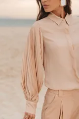 Camisa color beige de corte clásico, con cuello camisero, mangas largas abullonadas y cierre frontal con botones.