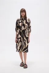 Vestido tipo camisa de corte holgado, con estampado de hojas en tonos marrones y beige. Presenta cuello camisero, cierre frontal con botones y mangas largas.
