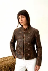 Chaqueta de cuero estilo militar en color cognac con acabado envejecido. Presenta cuello mao, cierre frontal con cordones y detalles de trabas horizontales con botones metálicos grabados.