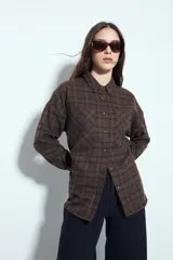 Camisa de corte relajado tipo leñadora con estampado de cuadros en tonos marrones y verdes. Presenta cuello clásico, cierre frontal con botones y bolsillos delanteros.