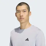 Remera deportiva Adidas de manga corta, color gris claro, con cuello redondo y diseño de las tres rayas características de la marca en color negro sobre los laterales. Presenta el logo de la marca en el pecho.