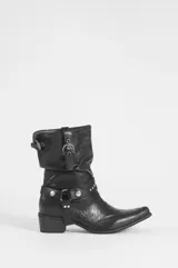 Bota corta de cuero vegano color negro, con taco cuadrado y punta fina. Presenta correas con tachas plateadas, hebillas y argollas metálicas decorativas alrededor de la caña y el tobillo.