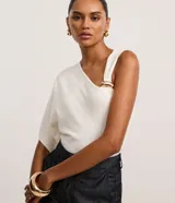 Blusa de punto color blanco marfil, con diseño asimétrico de una manga corta caída y un hombro al descubierto con tirante ancho, decorado con una pieza metálica dorada. Cuenta con escote en V y corte recto.