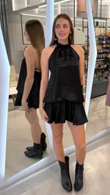 Vestido corto negro de cuello halter con acabado satinado, espalda descubierta y falda evasé con volados.