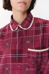 Camisa de corte holgado en color bordó con estampado de cuadros y monograma. Presenta cuello redondo con borde de puntilla, bolsillo frontal con detalle de puntilla, cierre frontal con botones y puños con terminación en puntilla.