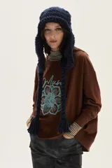 Buzo oversize de felpa color marrón con bordado frontal de una flor estilizada y la palabra "Muse" escrita en cursiva en color celeste.