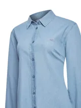 Blusa de denim color celeste, confeccionada en algodón orgánico, con cuello camisero, cierre frontal de botones y manga larga. Presenta un pequeño parche bordado en el pecho.