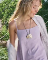 Collar artesanal con dije central de metal con textura orgánica irregular que evoca una ostra. El dije está montado sobre un cordón de algodón natural, permitiendo un uso versátil y regulable.