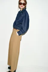 Chaqueta estilo bomber confeccionada en tejido denim azul oscuro. Presenta cuello solapa, cierre frontal con cremallera, mangas largas y bajo elástico. Incluye bolsillos delanteros de plastrón con solapa y botones.