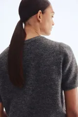 Buzo de punto fino color gris oscuro, con cuello redondo y manga corta. Presenta remates acanalados en cuello, puños y bajo.