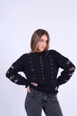 Sweater de punto negro con diseño de ochos, cuello redondo y detalles bordados a mano en color rosado en el frente y las mangas. Presenta un corte boxy con elástico ancho en la cintura y los puños.