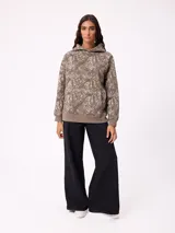 Canguro con capucha de corte holgado, estampado con diseño de ramas en tonos marrones y beige. Presenta bolsillo frontal tipo canguro, puños y ruedo en tejido rib elástico, y logo de la marca bordado en el pecho.