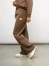 Pantalón de corte recto confeccionado en felpa, con cintura elástica ajustable mediante cordón y bolsillos laterales. Presenta un diseño minimalista con el logo de la marca sutilmente bordado en la parte frontal.