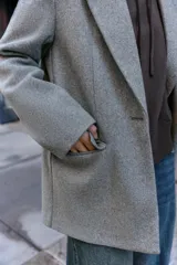 Blazer de corte recto y diseño minimalista, confeccionado en tejido de paño suave color beige. Presenta cuello con solapas clásicas, cierre frontal con un solo botón y dos bolsillos delanteros con solapa.