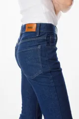 Pantalón de jean azul oscuro, corte acampanado (flare) de tiro alto, con costuras visibles en contraste y bordados tonales en la parte inferior de las piernas. El ruedo es deshilachado.