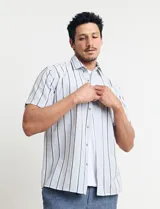 Camisa de manga corta con rayas verticales en tonos celeste, blanco, tostado y negro. Tiene cuello clásico, cierre con botones y bolsillo en el pecho.