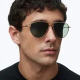 Lentes de sol estilo aviador con montura metálica fina en color dorado y lentes polarizadas en tono verde oscuro. Presentan un diseño clásico con doble puente y terminales de patillas en acetato.