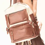 Mochila de cuero vacuno con diseño bicolor en tonos off-white y tabaco texturado. Presenta un formato estructurado con dos bolsillos frontales con cierre, compartimentos laterales y correas laterales decorativas con hebillas metálicas. Incluye cierre principal superior, correas de hombro regulables y asa superior reforzada.